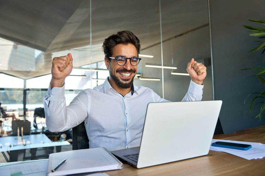 Professional happy business man celebrating success looking at laptop in office.