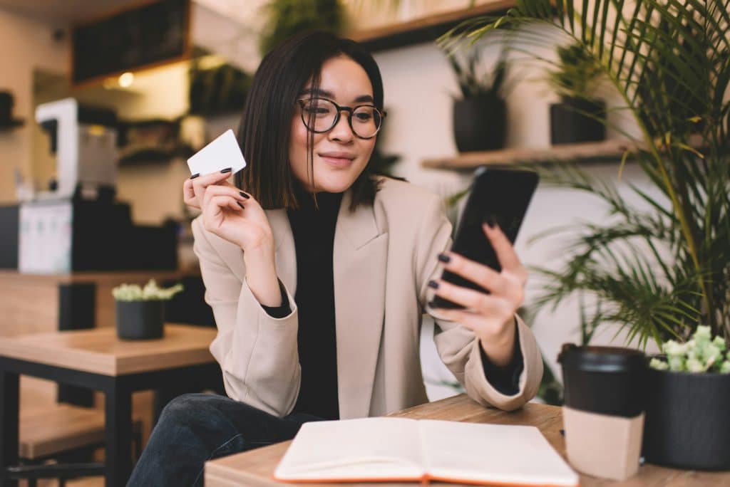 Girl with business card using smartphone in cafe