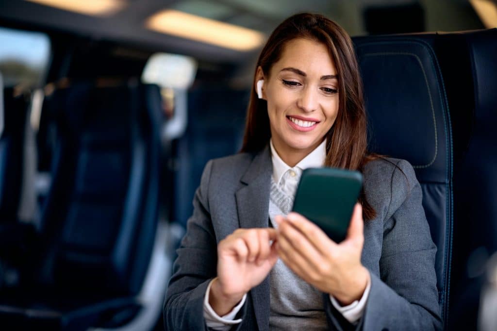 Happy businesswoman texting on mobile phone while traveling by train.