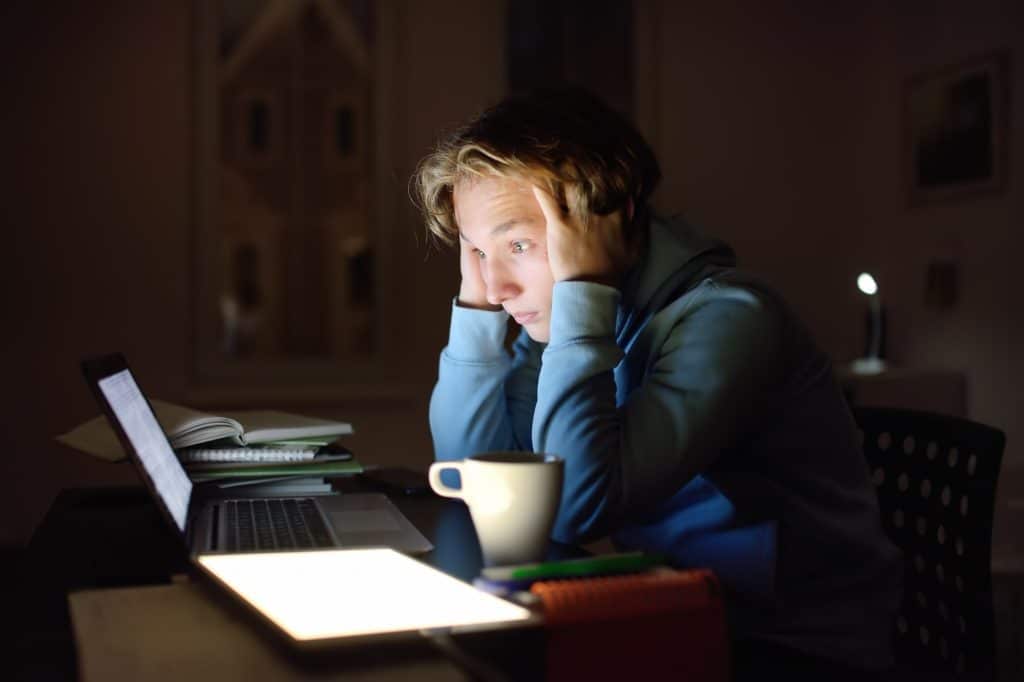 Shocked teenger studying night at home with laptop and tablet pc.