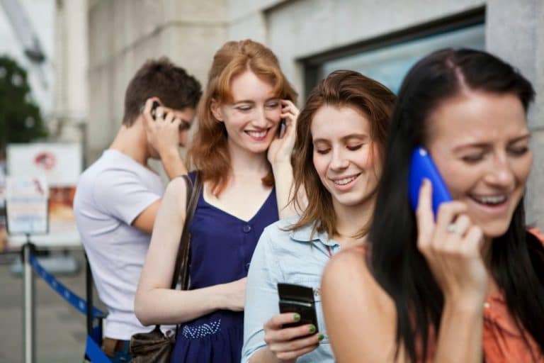 Four people in a queue, all using mobile phones